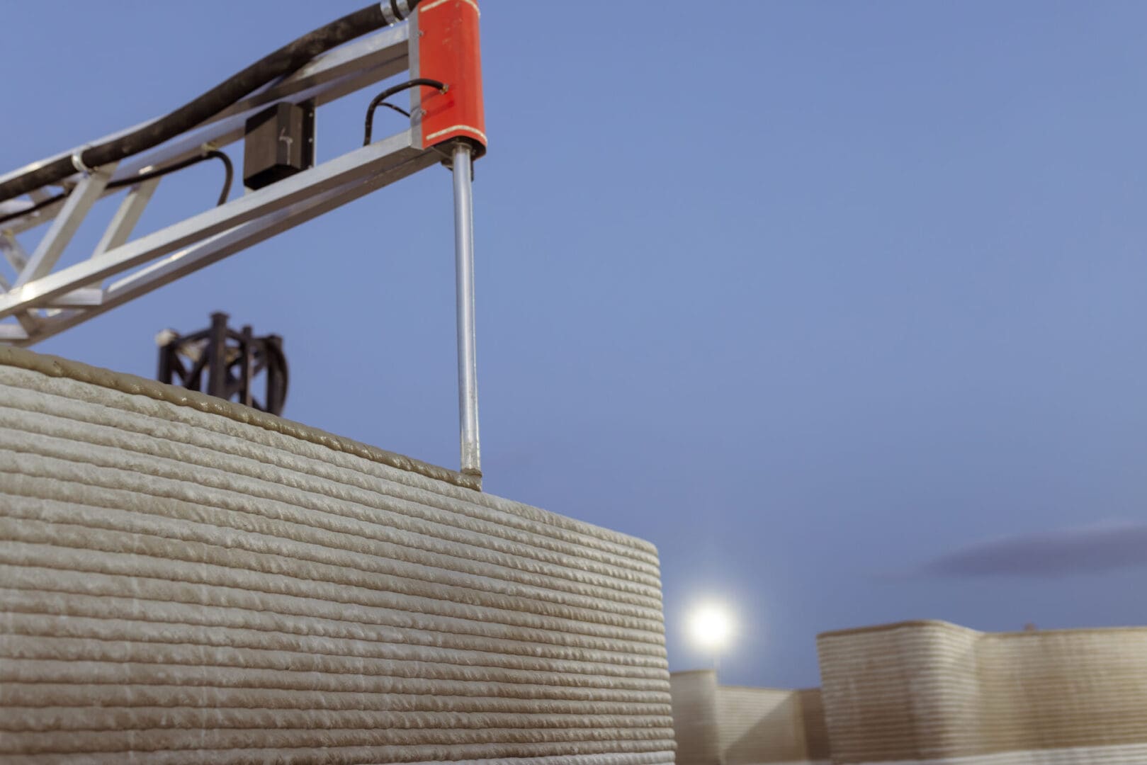 3D printer constructing a concrete wall under a clear sky.